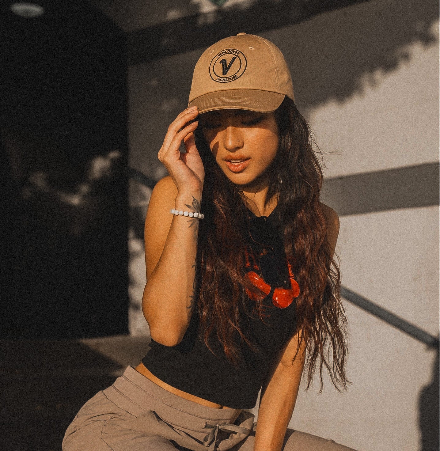 Female model wearing the sands and black Elation relaxed-fit hat by Vancouver Signature outdoors in a sunny setting.