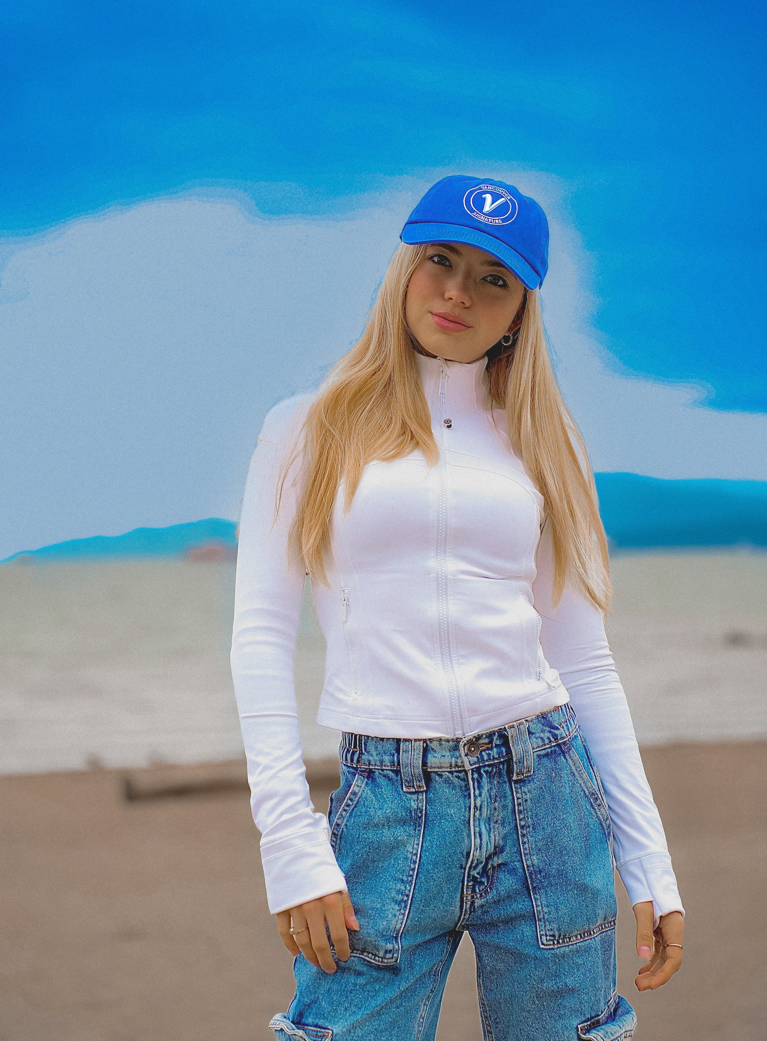 Female model on a beach wearing the pacific and white Elation relaxed-fit hat by Vancouver Signature 