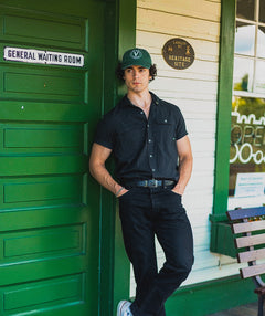 Male model wearing the pine and white Elation relaxed-fit hat by Vancouver Signature outdoors by a building
