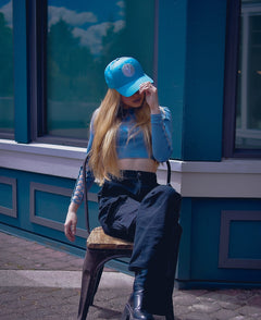Woman sitting on a chair and adjusting the Vancouver Signature Listo structured hat in lagoon and white