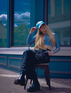 Woman sitting on a chair and wearing the Vancouver Signature Listo structured hat in lagoon and white